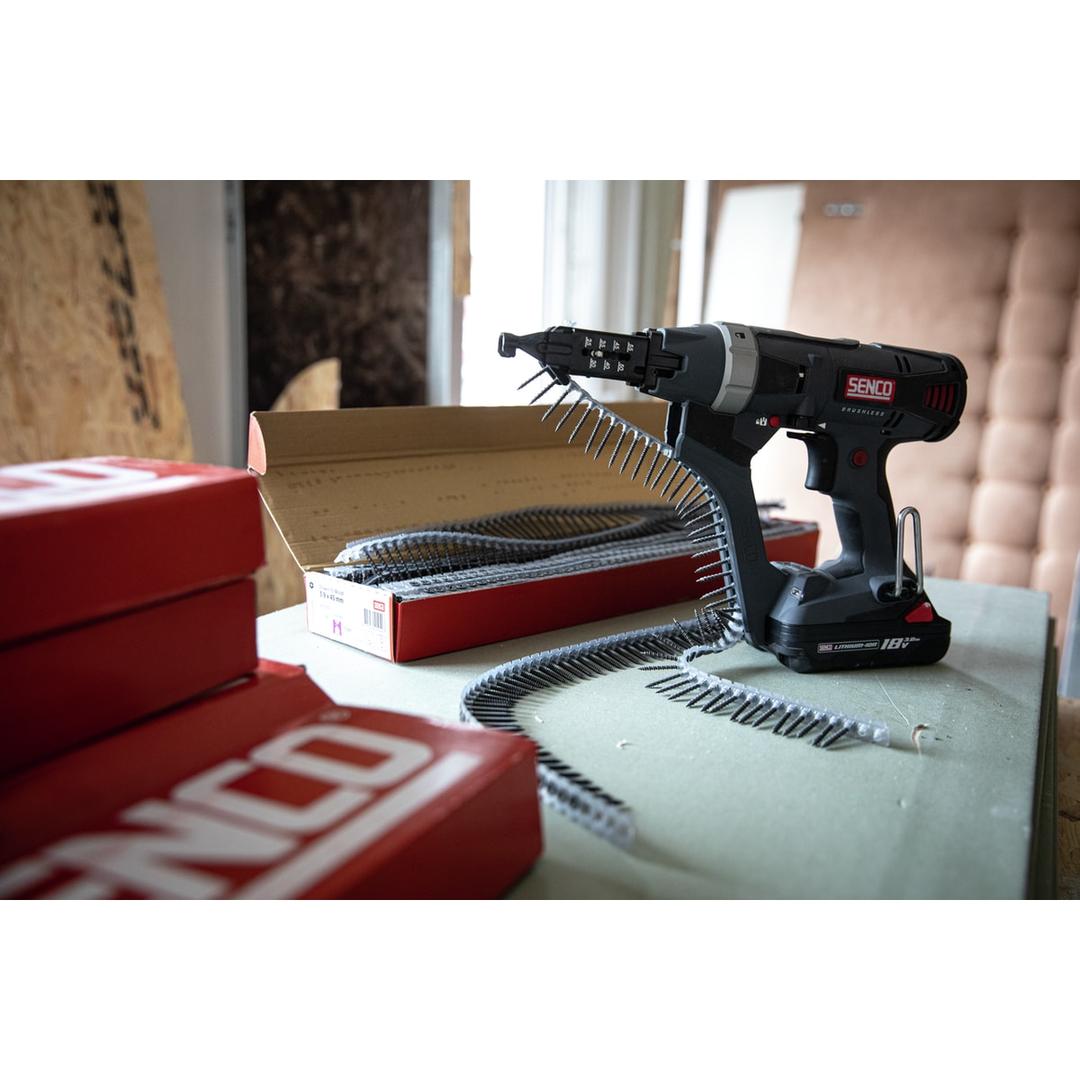 Visseuse en bande sur batterie DURASPIN DS525-18V SENCO — Visseuse en bande SENCO DS525-18V posée sur un établi, bande de vis chargée et cartons de recharges