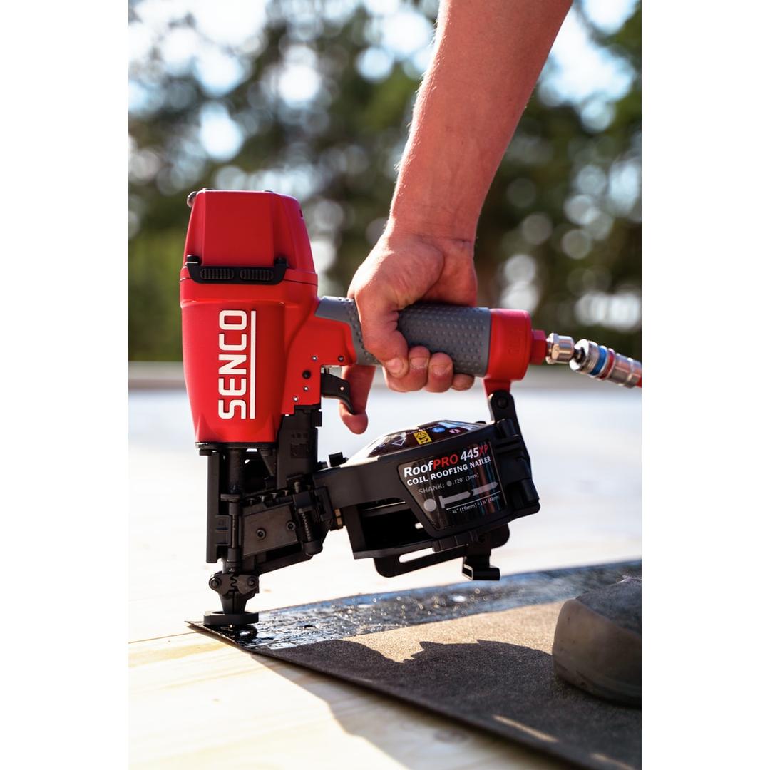 Cloueur roofing pneumatique ROOFPRO 445 XP SENCO — Cloueur roofing SENCO ROOFPRO 445 XP tenu en main sur une toiture, tuyau d'air raccordé