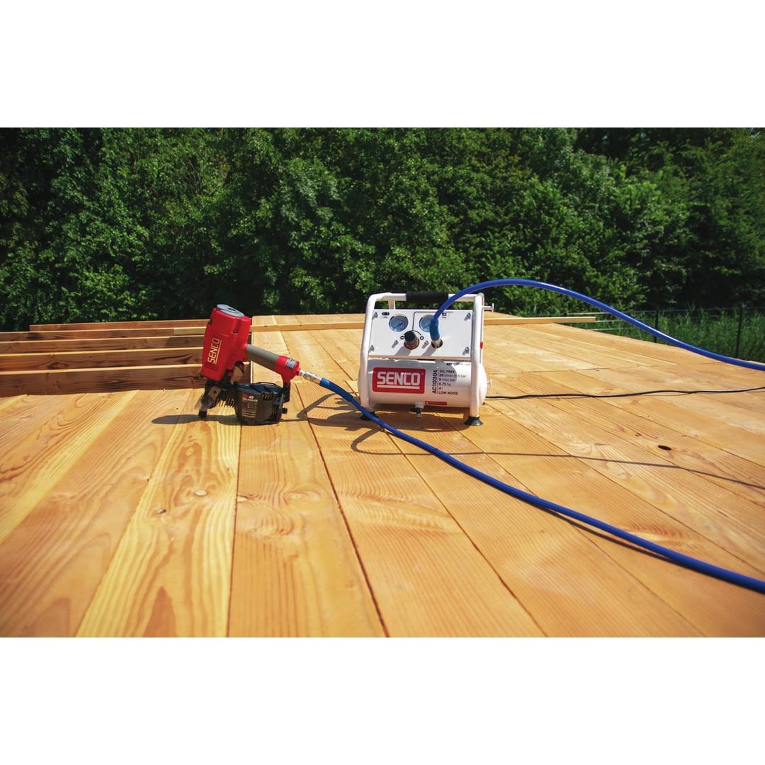 Compresseur SENCO AC10304 discret sans huile SENCO — Compresseur SENCO AC10304 sans huile et cloueur pneumatique posés sur une terrasse bois, tuyau bleu déroulé