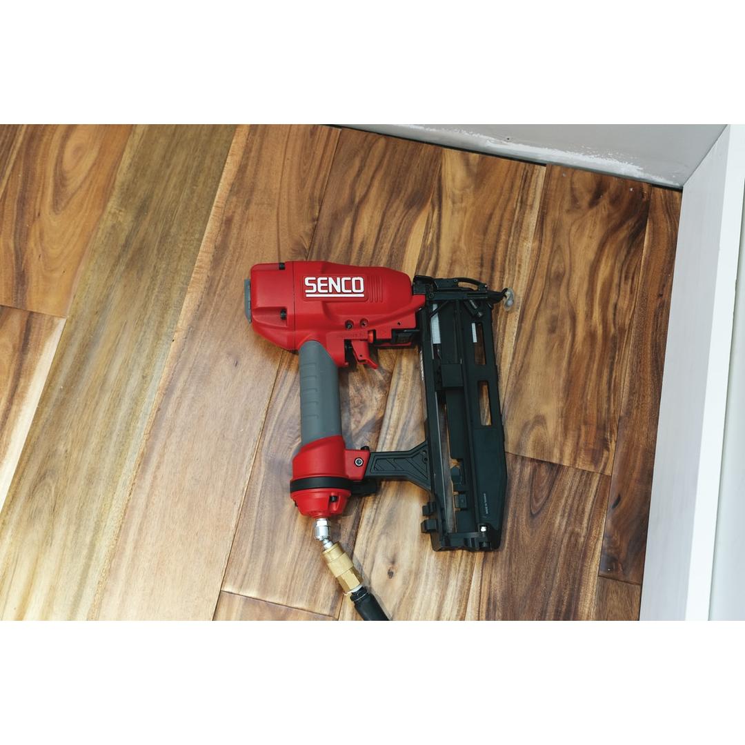 Cloueur pneumatique FINISHPRO 16XP SENCO — Cloueur SENCO FinishPro 16XP 32-65 mm posé sur un parquet foncé, tuyau d'air et raccord laiton