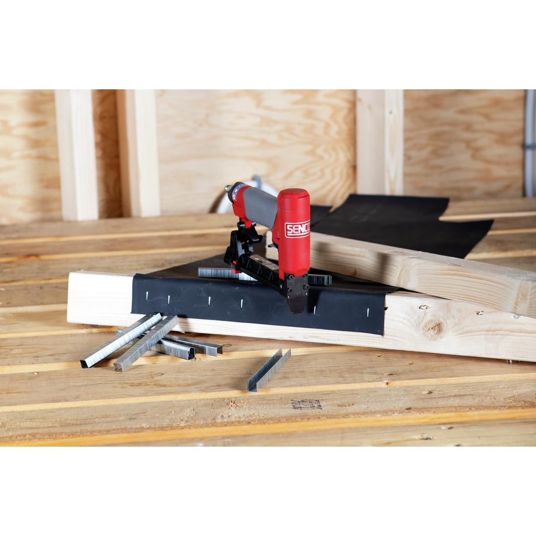 Agrafeuse pneumatique SFT10XP A SENCO — Agrafeuse SENCO SFT10XP A 6-12 mm posée sur une membrane agrafée, charpente bois en arrière-plan