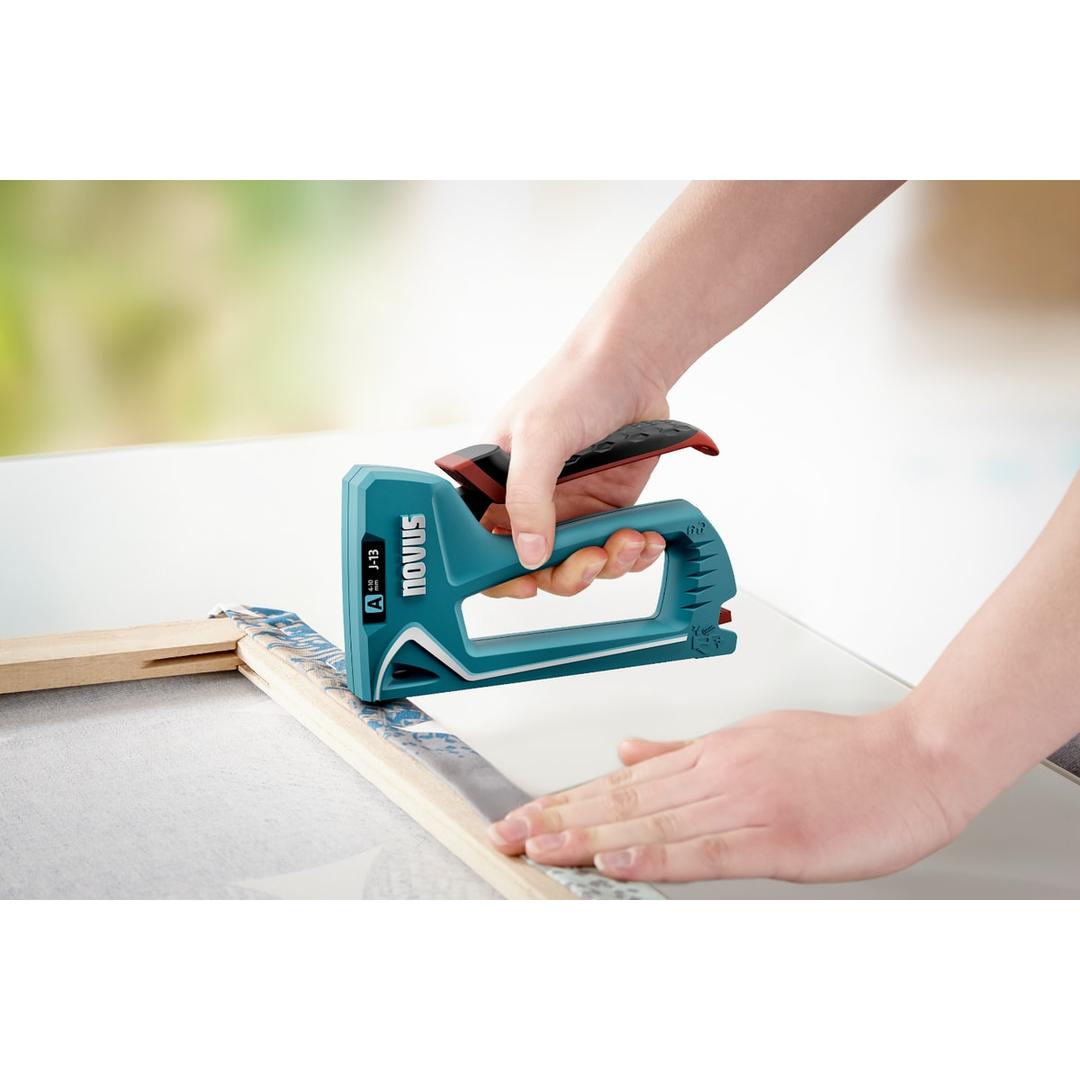 Agrafeuse manuelle J-13 NOVUS — NOVUS agrafeuse manuelle J-13 — agrafage d'une toile sur un châssis bois, main serrant le levier