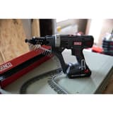 Visseuse en bande sur batterie DURASPIN DS525-18V SENCO — Visseuse en bande SENCO DS525-18V posée devant un panneau OSB, longue bande de vis en boucle