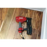 Cloueur pneumatique FINISHPRO 16XP SENCO — Cloueur SENCO FinishPro 16XP 32-65 mm posé sur un parquet foncé, tuyau d'air et raccord laiton