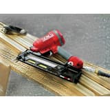 Cloueur pneumatique FINISHPRO 42XP ,5 mm DUAL/RESTR SENCO — Cloueur SENCO FinishPro 42XP 32-63,5 mm posé sur une moulure en bois clair, flexible d'air raccordé