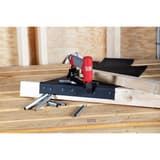Agrafeuse pneumatique SFT10XP A SENCO — Agrafeuse SENCO SFT10XP A 6-12 mm posée sur une membrane agrafée, charpente bois en arrière-plan